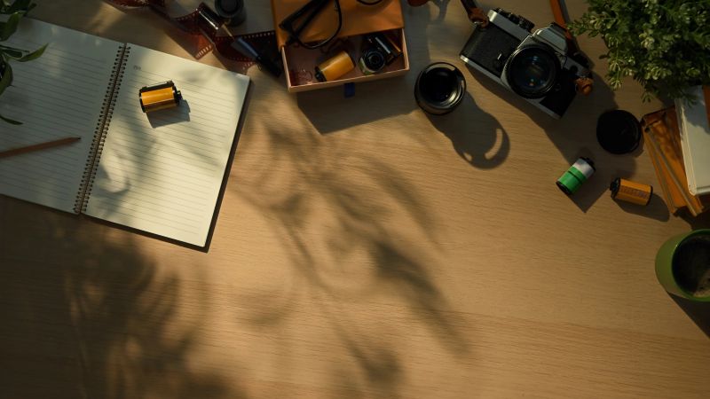 Creative workspace with vintage camera, notebook, and coffee cup in warm morning sunlight.