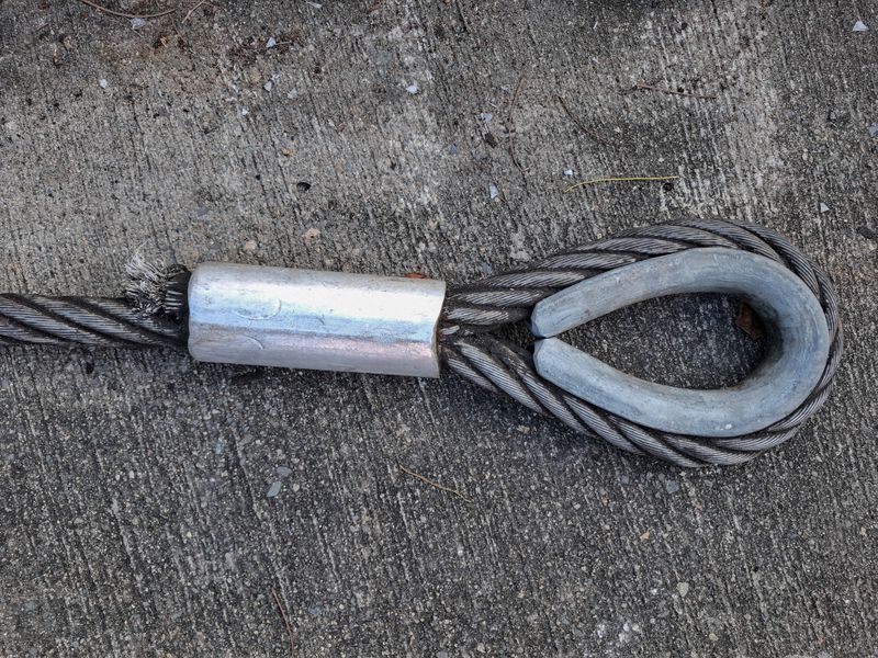 Close-up of a steel wire rope sling with thimble eye and pressed ferrule sleeve on a concrete surface. Heavy lift, rigging, construction, and safety equipment