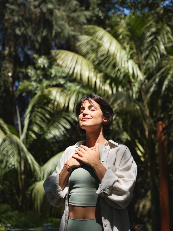 Woman enjoying sunlight with hands on chest outdoors.