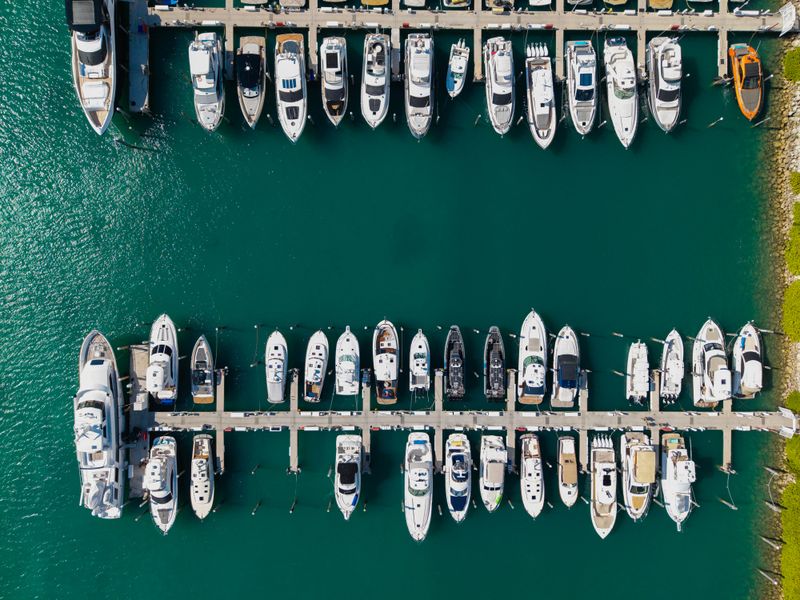 Aerial view of luxury yachts docked at marina. Top-down drone shot of yachts. Boats and sailboats line the scenic seashore. Yacht cruising along the coastline. Harbor filled with vessels at dawn