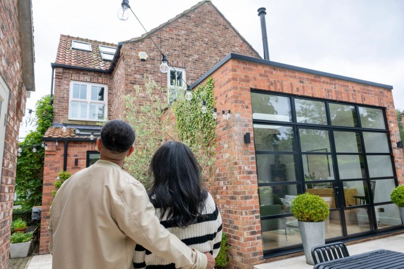 Couple in back garden looking at house, man with arm around woman, home improvement, building, extension, house purchase