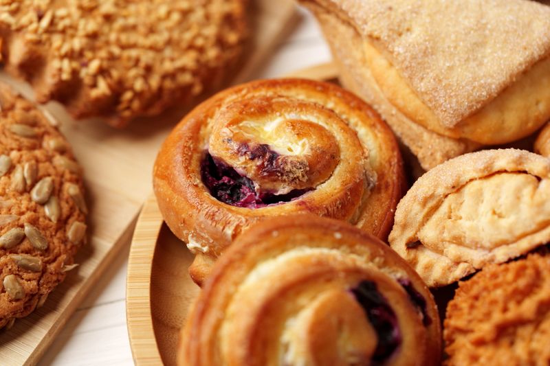Various delicious baked goods, including cinnamon rolls and cookies, are arranged beautifully on a wooden platter in a warm kitchen environment, showcasing homemade treats.