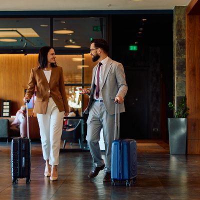 Two business travelers walking with suitcases in a hotel lobby.