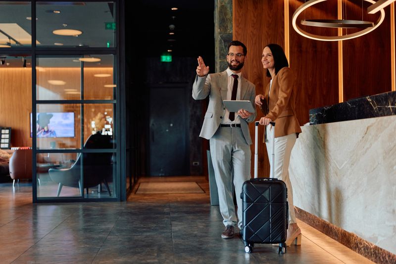 Happy business travelers consulting with a concierge at the hotel reception, getting directions for their next meeting or discussing upcoming plans in a luxurious executive lounge environment