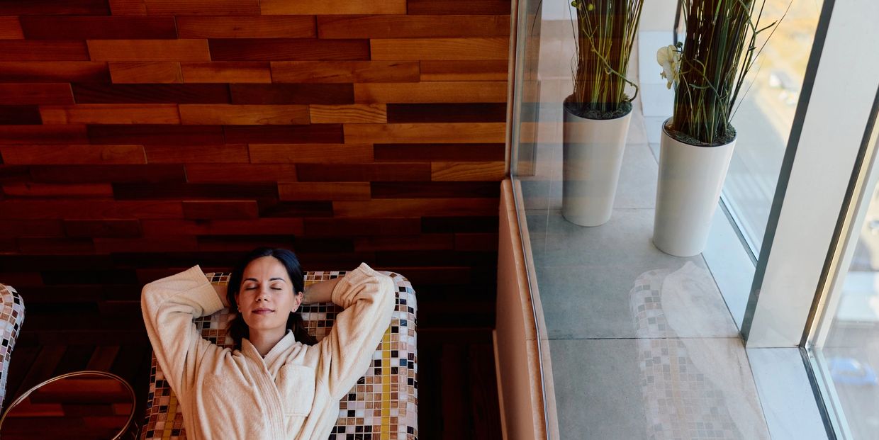 Woman relaxing in a robe on a mosaic lounge chair by a large window.