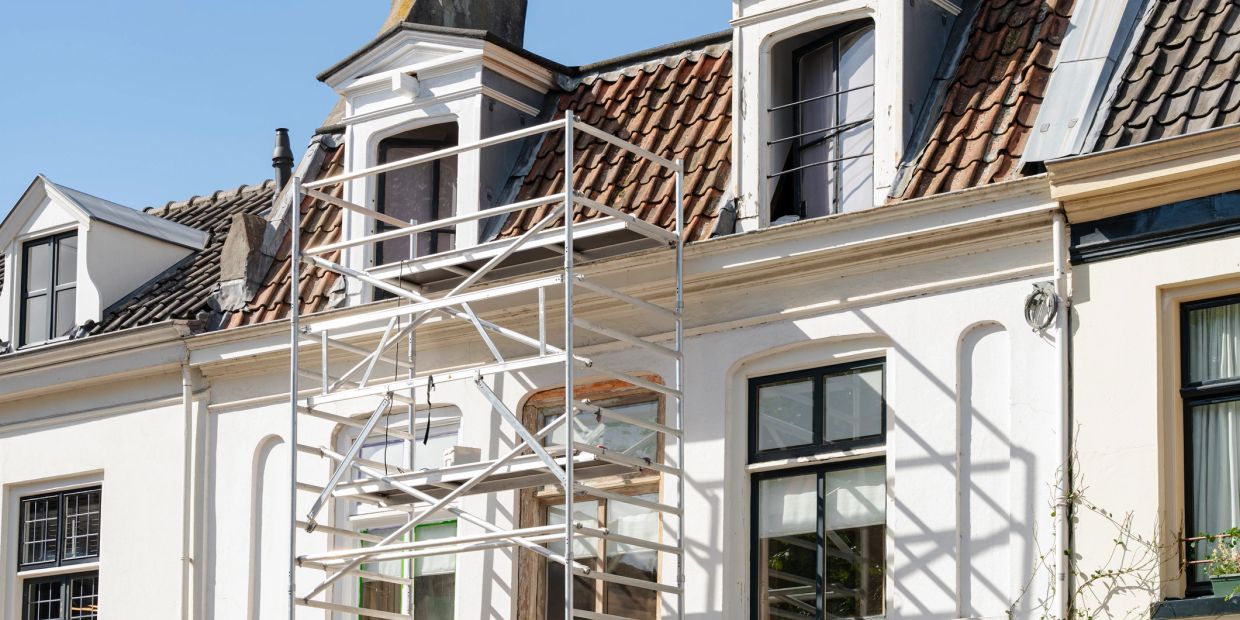 Scaffolding in front of a white house with tiled roof.