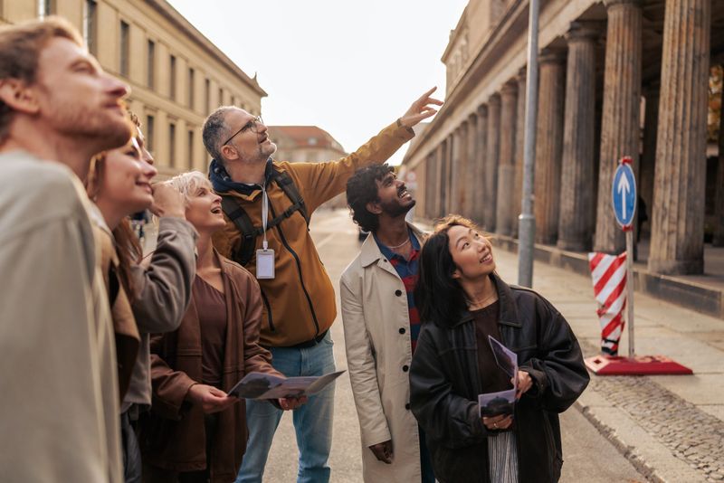 A guide points to Kolonnadenhof and shares information with a multicultural group of tourists during a city tour in Berlin. The group stands outdoors, appreciating architecture, history, and cultural exploration.