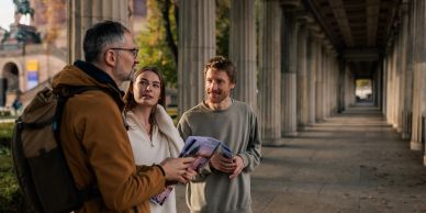 Three people standing and talking outdoors under a covered walkway.