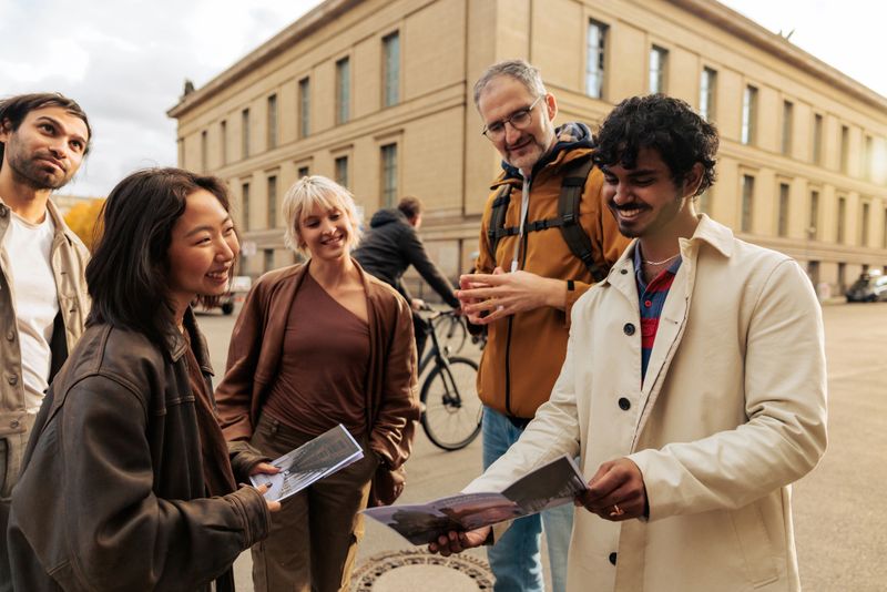 A male tour guide with a backpack talking with a diverse group of tourists while looking at a city map in Berlin, Germany. They plan their sightseeing route together, representing teamwork, travel, and cultural exploration.