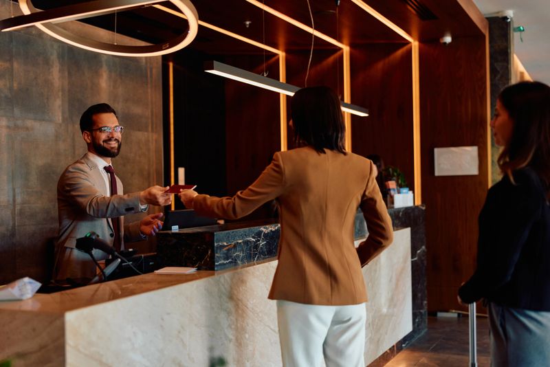 Smiling hotel receptionist exchanging a passport with a female guest at the front desk, highlighting professional hospitality service and welcoming travelers to the modern lobby environment