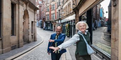Older couple dancing joyfully on a cobblestone street.
