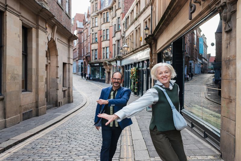 A three-quarter length shot of a stylish senior couple dancing down a historic cobblestone street in Newcastle Upon Tyne. They are both well-dressed, enjoying their long weekend away together.Videos of this scenario are available