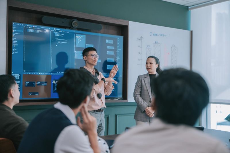 Deaf chinese male employee presenting with support from a sign language interpreter during a business meeting, promoting workplace inclusivity, accessibility, and collaboration. Location: Kuala Lumpur.