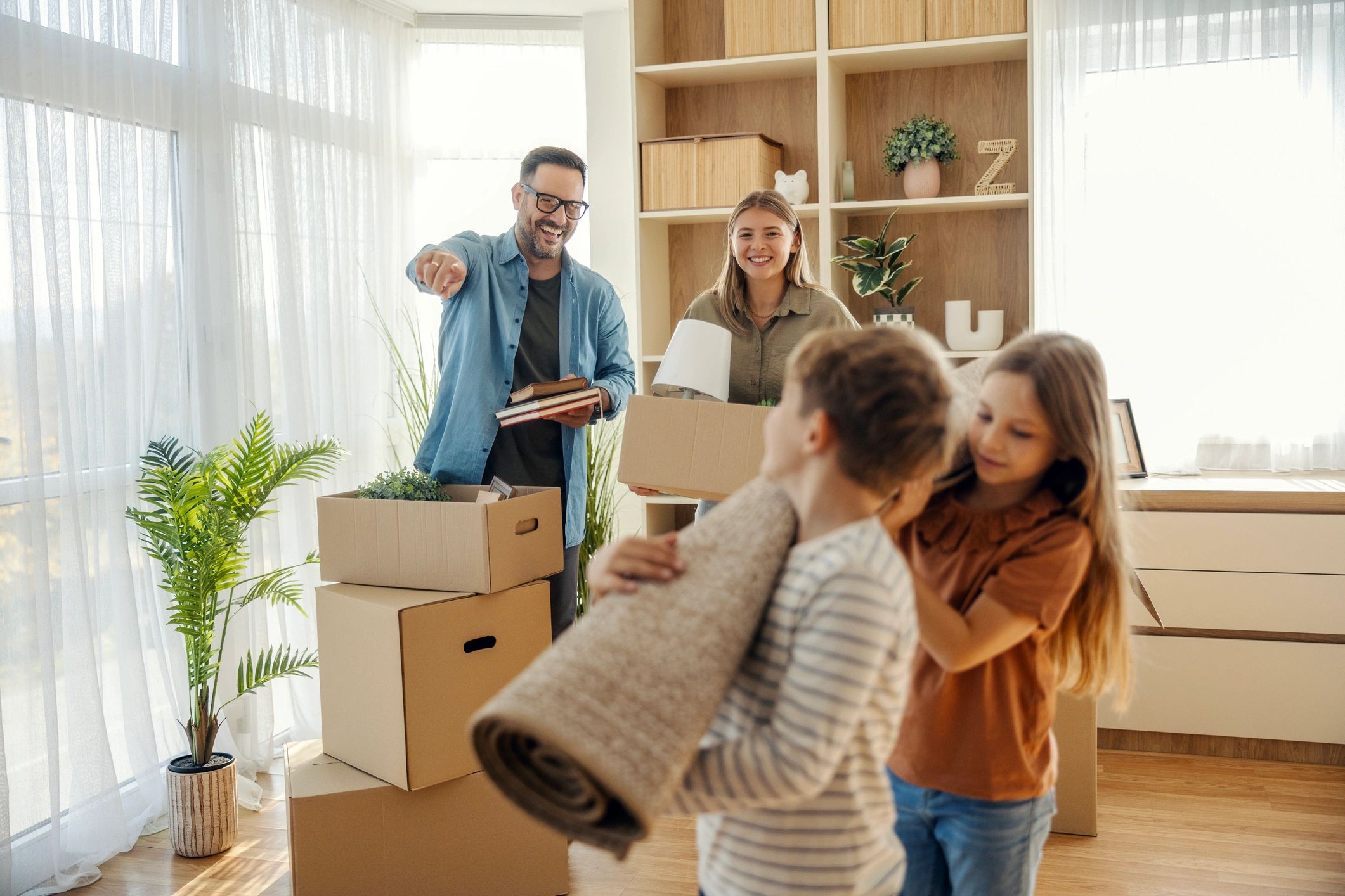 A happy family of four moving into a new home, surrounded by cardboard boxes. In the background, a s