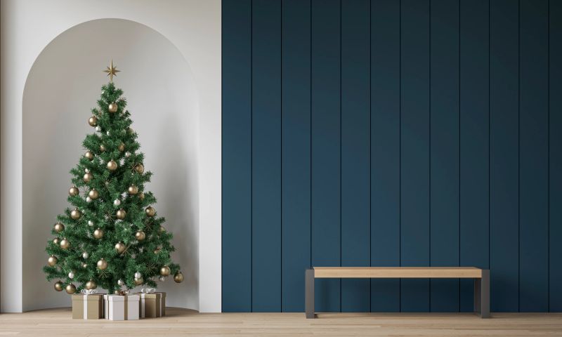 Modern living room decorated for Christmas with a beautifully adorned tree placed in a wall niche and surrounded by wrapped gifts. A modern wooden bench with metal legs placed against a deep blue shiplap wall with copy space, creating a stylish and festive atmosphere. Natural light and minimalistic decor enhance the warm, elegant holiday mood. 3D erendered image