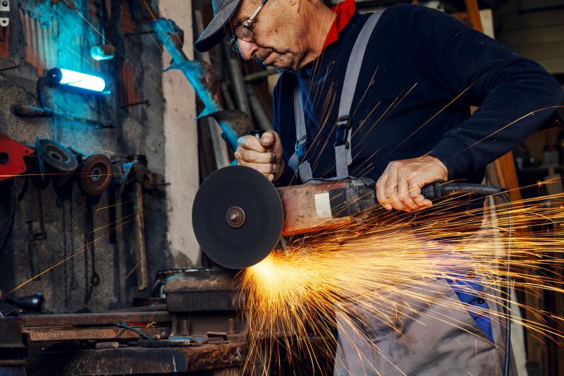 Male metalworker using angle grinder tool on metal workpiece. Flying golden sparks illuminate the intense work