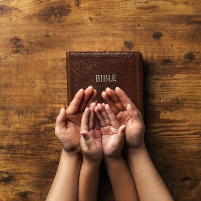 Hands of adult and child near a Bible on wooden surface.