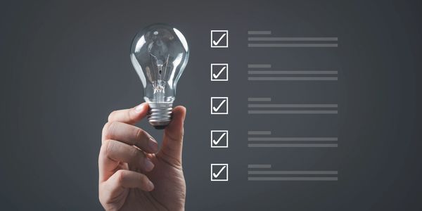 Hand holding a light bulb next to a checklist with five checked boxes.