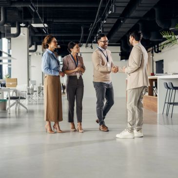 Two men shaking hands while two women watch in an office.