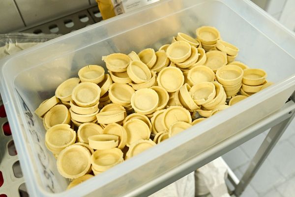 A clear plastic bin full of stacked, pre-baked, empty mini tart shells.