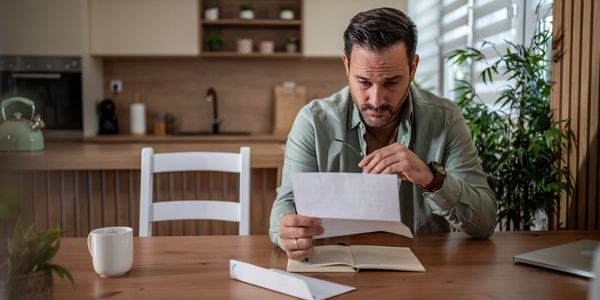Man reading a letter at a wooden table in a modern kitchen.