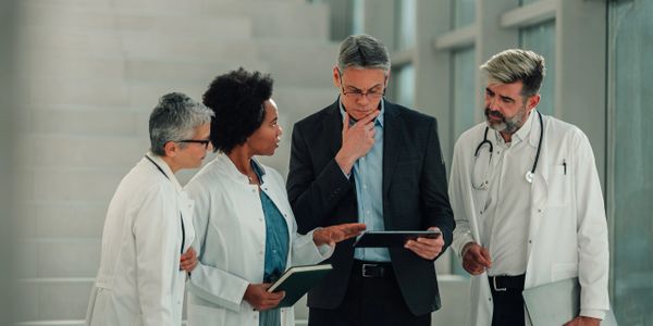 A group of doctors and a businessman discussing medical data on a tablet.