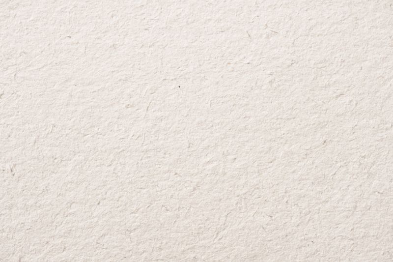 Macro image of white handmade paper with a soft, fibrous texture and natural irregularities across the surface.