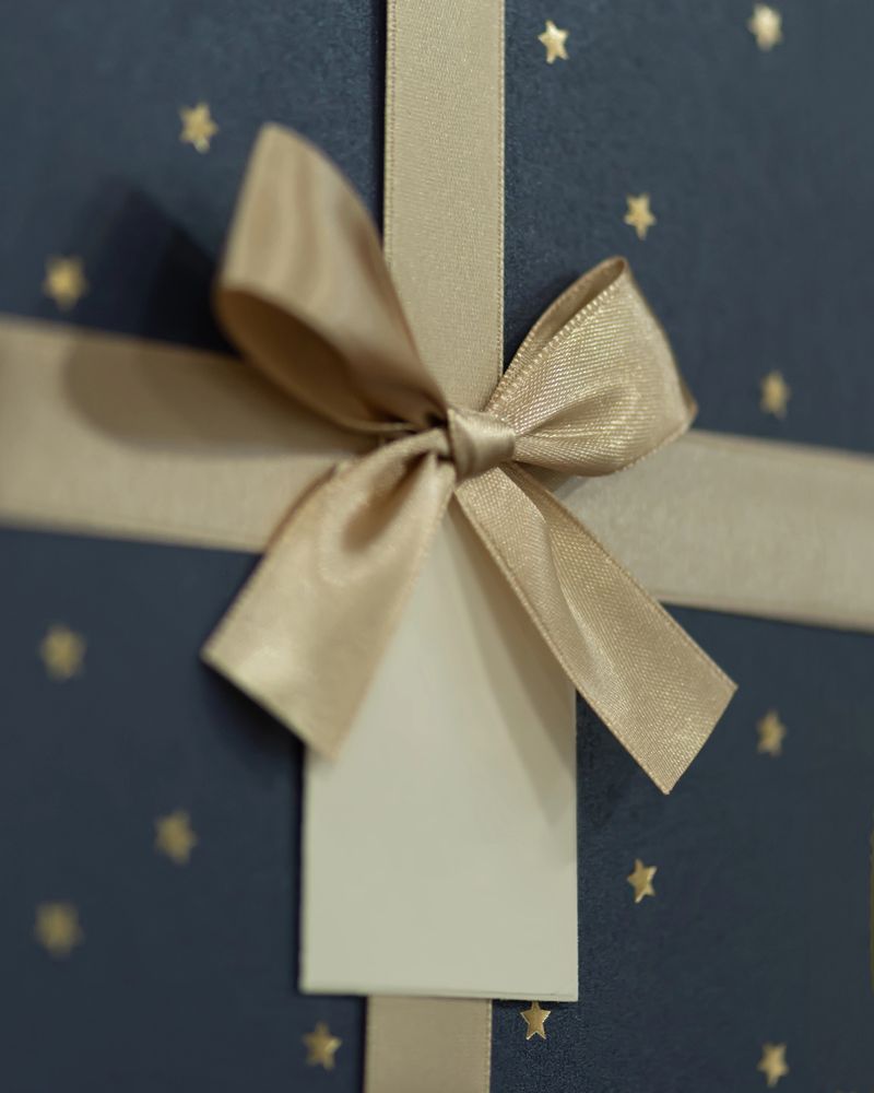 Close up of luxury present box tied with golden satin ribbon and empty gift tag. Stylish holiday packaging concept for celebration, birthday, or Christmas design.