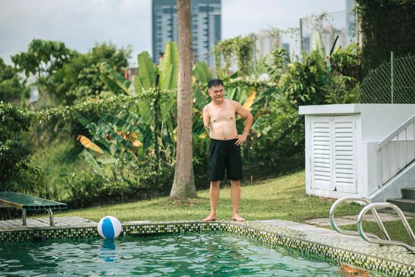 A backyard swimming pool with lounge chairs and patio furniture under a tiled roof.