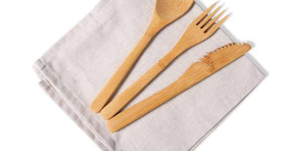 Bamboo spoon, fork, and knife on a folded beige cloth napkin.