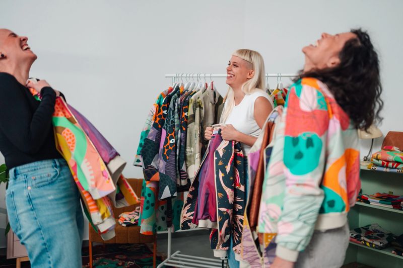 Three women friends experiencing joy and laughter while shopping for unique clothing in a vibrant boutique