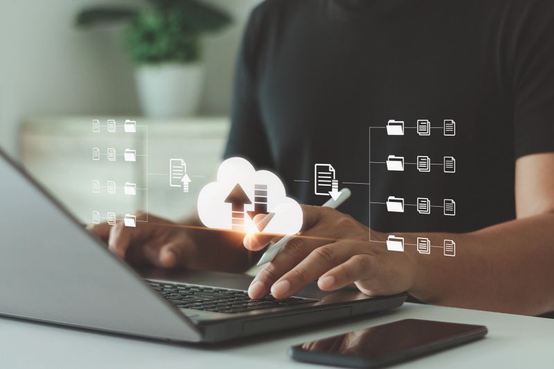 Businessman using laptop with digital cloud storage interface, data upload and file sharing system for online business. Concept of cloud computing, data management and technology innovation.