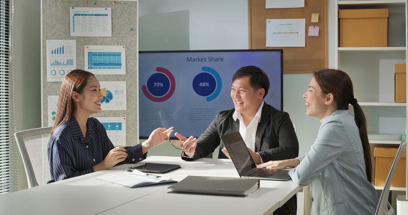 Group of cheerful Asian colleagues smiling and laughing together during a meeting in a modern office. Positive work culture, business team bonding, and relaxed corporate atmosphere.