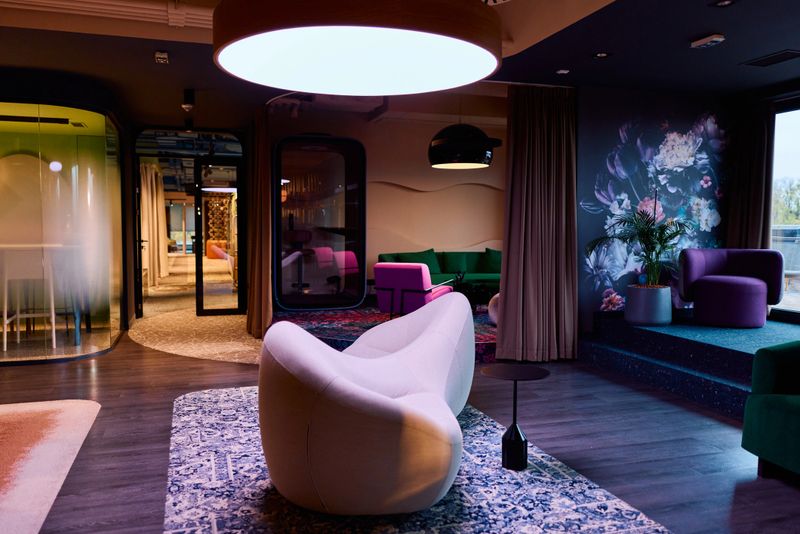 Modern office lounge area with diverse, colorful furniture, acoustic pods, and a vibrant floral wall mural, providing a comfortable and inspiring collaborative workspace