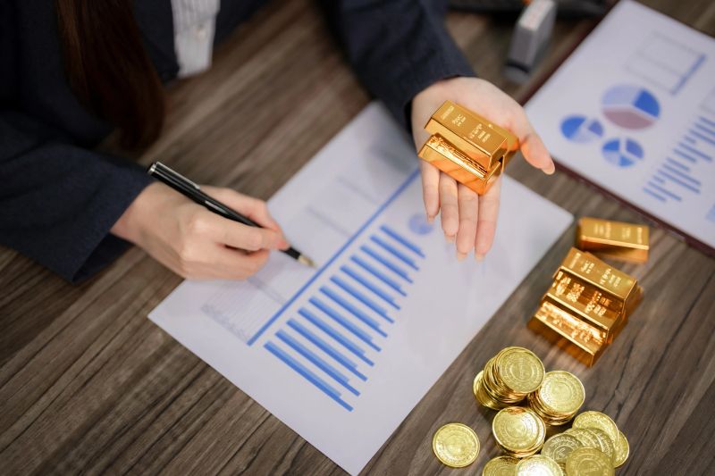 Adult hands engage in meticulous financial analysis of gold investments. Reviewing market charts and holding precious metal bars for wealth management strategy.