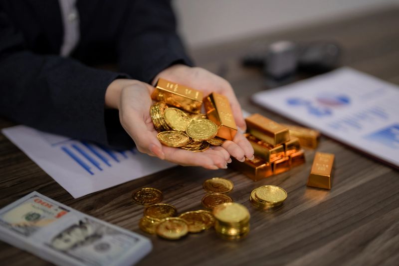 Adult hands hold lustrous gold bars and precious coins. Financial documents and cash signify secure investments and strategic wealth accumulation for future prosperity.