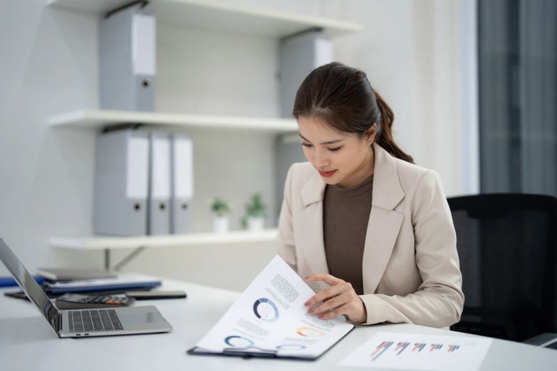 Focused Asian businesswoman reviews crucial property sales statistics and market analysis in a modern office environment for strategic growth