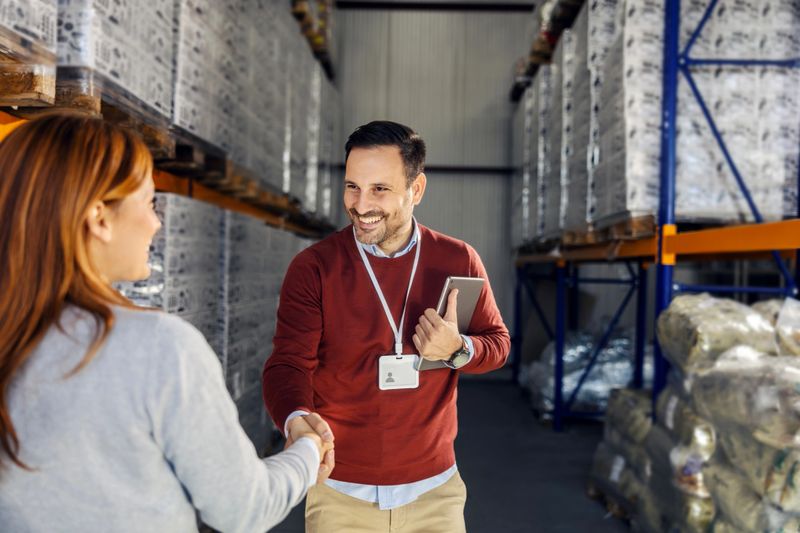 Business associates concluding a deal with a handshake, symbolizing partnership, agreement, and successful logistics operations in a warehouse