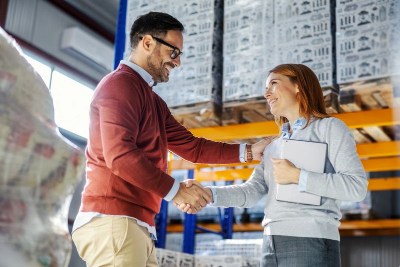 Business partners shaking hands in a distribution warehouse, closing a deal and celebrating a successful partnership