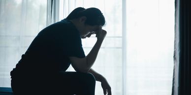 A person sitting in silhouette, appearing deep in thought or sadness.