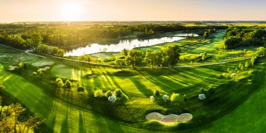 Aerial view of a golf course at sunset with lush greenery and water features.