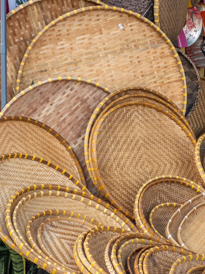 Intricate patterns of natural bamboo weaving create a rustic, earthy backdrop. A vibrant composition of traditional handcrafted trays and baskets, showcasing artisanal texture and warm tones, offers a