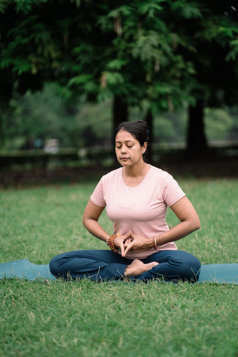 Serene moment of meditation outdoors — a woman sits in a meditative posture on the grass, focusing on calm breathing and mindfulness in nature. Ideal concept for health, yoga, and mental well-being.