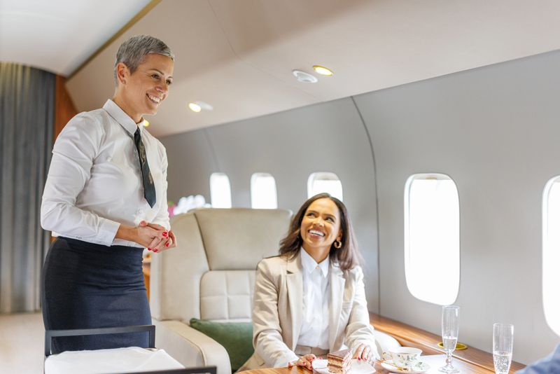 Flight attendant offering dessert to a smiling businesswoman on a luxury private jet