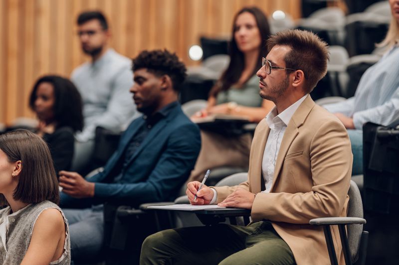 Group of adults attending a business or educational seminar, listening attentively to a speaker and taking notes on a notepad