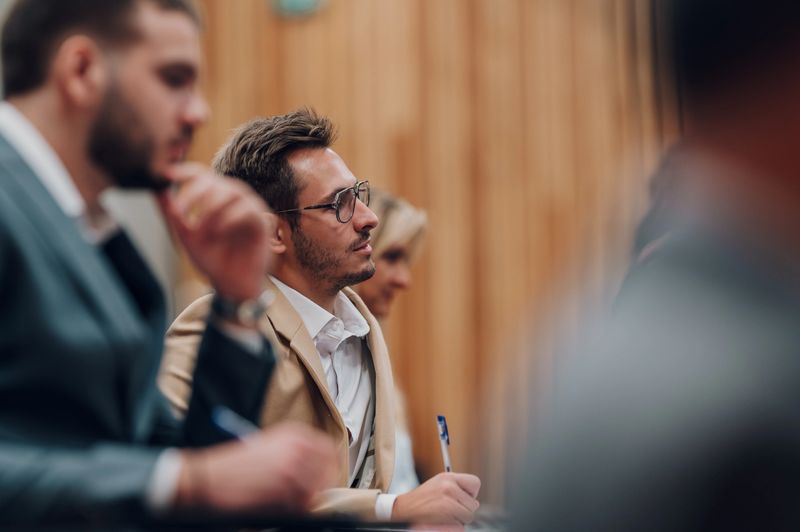 Young man wearing glasses intently listening while attending a business conference or educational lecture. Learning and development concept