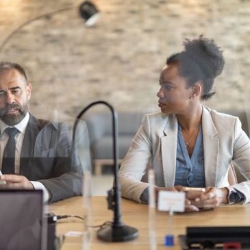 Two professionals sitting apart with a transparent divider between them.