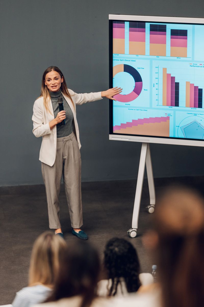 Young adult businesswoman using a large screen to present financial data and analytics to a group of colleagues