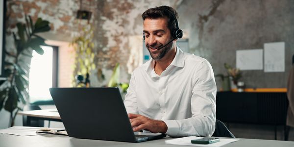 Man in white shirt using laptop with headset in a modern office.