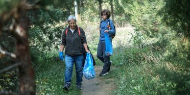 Two people picking up trash on a forest path.